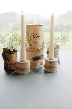 three candles are placed in birch logs and tied with twine, on a table