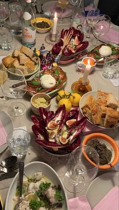 a table filled with plates and bowls of food next to candles on top of a table