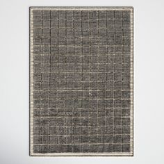 a gray and white area rug with squares on the bottom, in front of a white wall