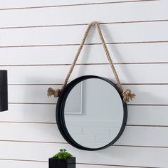 a round mirror hanging on the side of a white wall next to a potted plant