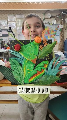 a young boy holding up a cardboard art piece