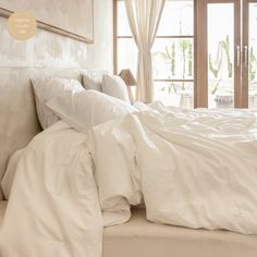 an unmade bed with white linens and pillows in front of a sliding glass door