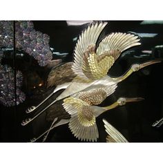 three metal birds on display in a glass case with purple and white flowers behind them