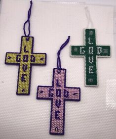 two cross shaped ornament hanging on a white cloth with green and pink trim