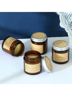 four jars of candles sitting on top of a white table next to a lace doily