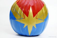 a blue and yellow painted pumpkin with a red star on it's top, sitting in front of a white background