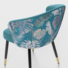 an upholstered chair with blue fabric and tropical print on the back, along with black legs