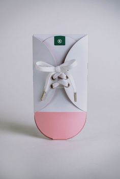 a white and pink shoe box with a bow on the top, sitting in front of a gray background