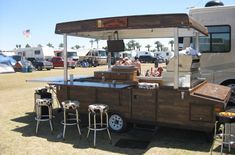 an outdoor food cart with people sitting at the table in front of it and parked on grass