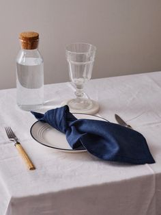 a white table topped with a blue napkin and a bottle filled with water next to a fork