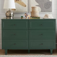 a green dresser with two pictures on the wall above it and a lamp next to it