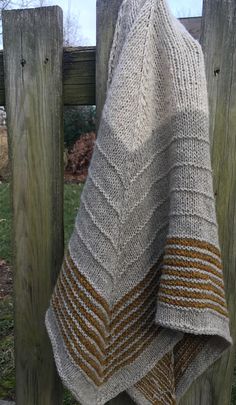 a knitted blanket hanging on a wooden fence