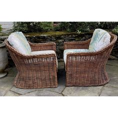 two wicker chairs sitting next to each other on a stone patio with potted plants in the background