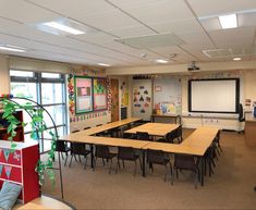 an empty classroom with desks, chairs and a projector screen in the corner