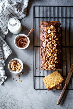 a loaf of chocolate cake sitting on top of a cooling rack next to bowls of nuts