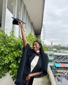 a woman wearing a graduation gown and holding her cap in the air while standing on a balcony