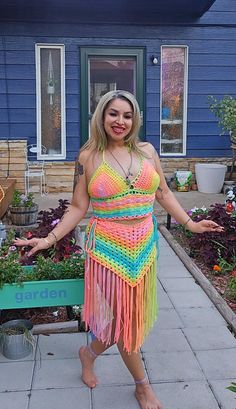 a woman standing in front of a house wearing a multicolored crochet dress