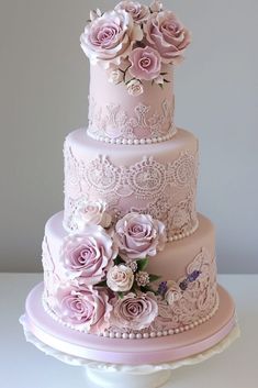 a three tiered cake with pink roses on top and white lace around the edges