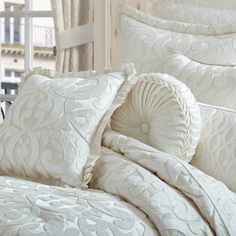 a bed with white comforters and pillows on top of it in front of a window