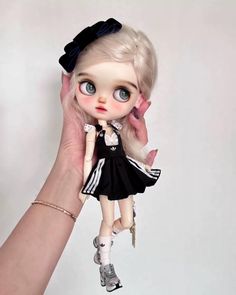 a doll is being held up by a person's hand, wearing a black and white dress