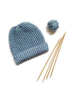 a blue knitted hat next to two knitting needles