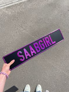 a person holding up a purple skateboard that says saabgirl on it and the word saabgirl written in pink