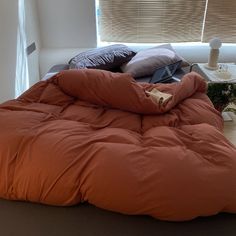 an orange comforter on top of a bed in front of a window with blinds