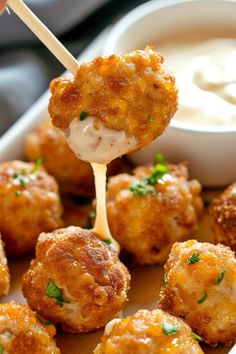 a close up of food on a stick with sauce in a bowl behind it,