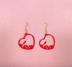 two red heart shaped earrings with the word love written in it on a pink background