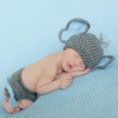 a baby wearing a crocheted hat and diaper sleeping on a blue blanket