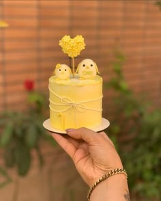 a hand holding a small yellow cake with two birds on top