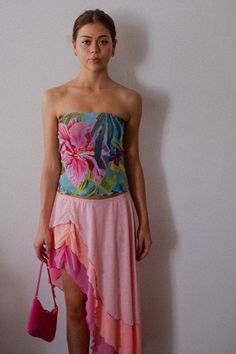 a woman standing in front of a white wall holding a pink purse and wearing a strapless dress