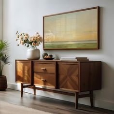 a painting hangs on the wall next to a wooden dresser with flowers in vases