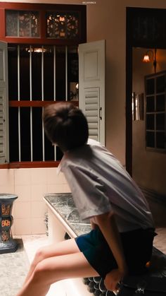 a woman sitting on top of a stove in front of a kitchen counter next to a window