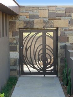 an iron gate in front of a stone wall with cactus growing on the side walk