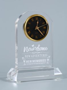 a clear glass clock with the words new home on it's face and gold hands