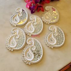 six white lace appliques sitting on top of a counter next to pink flowers