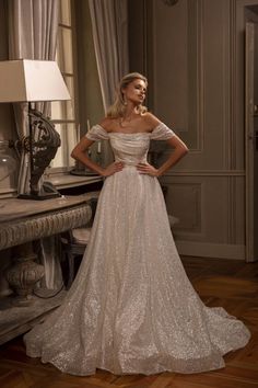 a woman in a wedding dress standing next to a table with a lamp on it