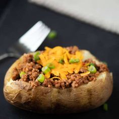 a close up of a baked potato with ground beef and cheese on top, next to a fork