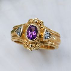 18K gold granulated ring with 7x5mm oval amethyst and 2- 4mm trillion cut aquamarines. The granulation runs down either side of the band resulting in a wider band measuring approximately 6.6mm in width. Currently size 6.75, but but each ring comes with free sizing and FREE SHIPPING! Unsure what ring size you are? It's always best to be sized by a professional jeweler, but if that is not available, you can use our special Ring Sizing Chart. Heirloom Yellow Gold Amethyst Ring With Accent Stones, Heirloom Amethyst Ring With Accent Stones, Heirloom Amethyst Birthstone Ring, Heirloom Gold Birthstone Ring With Blue Topaz, Gold Heirloom Style Blue Topaz Birthstone Ring, Heirloom Gold Blue Topaz Birthstone Ring, Heirloom Oval Multi-stone Amethyst Ring, Heirloom Multi-stone Oval Amethyst Ring, Vintage 14k Gold Amethyst Ring Hallmarked