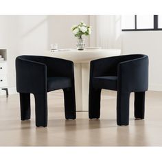 two black chairs sitting next to each other on top of a hard wood floor in front of a white table