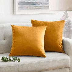 two yellow pillows sitting on top of a white couch next to a vase with flowers