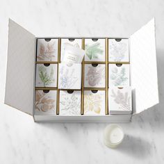 an open box with twelve cards and a candle on a marble countertop next to it