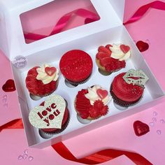 a box filled with red cupcakes covered in frosting and decorated with hearts