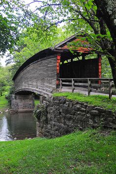 an old wooden covered bridge over a small stream in a park with green grass and trees