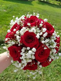 a bouquet of red roses and white baby's breath is held in someones hand