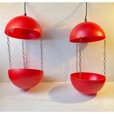 two red hanging bowls with chains attached to them on a white wall in front of a light fixture