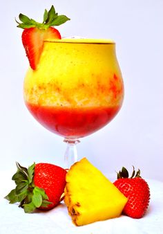 a glass filled with fruit sitting on top of a white table next to sliced strawberries