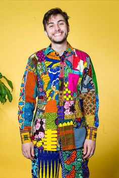 a man standing in front of a yellow wall wearing a multicolored shirt and pants