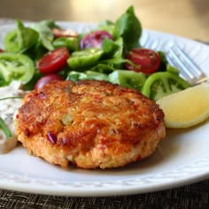 a white plate topped with meat patties next to a salad and a lemon wedge